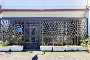 Une entrée fermée par un portail et agrémentée d’une clôture en métal décorative, de plantes en pot et d’un panneau bleu.