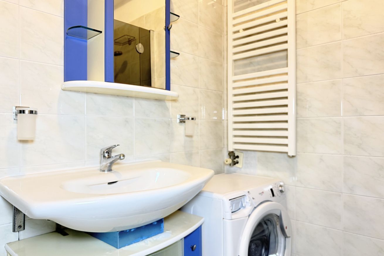 A bathroom with a sink, mirror, and a washing machine.