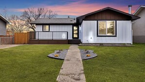 A modern two-story house with a front yard, a pathway, and a wooden fence. - Luxe 3BR • Sleeps 8 • King Beds • Steps to Train (Calgary)