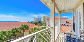 A balcony with a view of a coastal area, red-tiled roofs, and tall buildings in the distance.