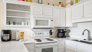 A kitchen with white cabinets, a microwave, a stove, a coffee maker, and a toaster. - Horizon South 55-304 (Panama City Beach)