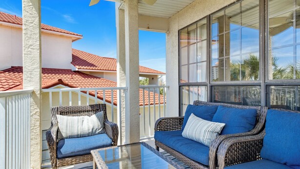 A covered outdoor seating area with wicker furniture and a glass table. - Horizon South 55-304 (Panama City Beach)