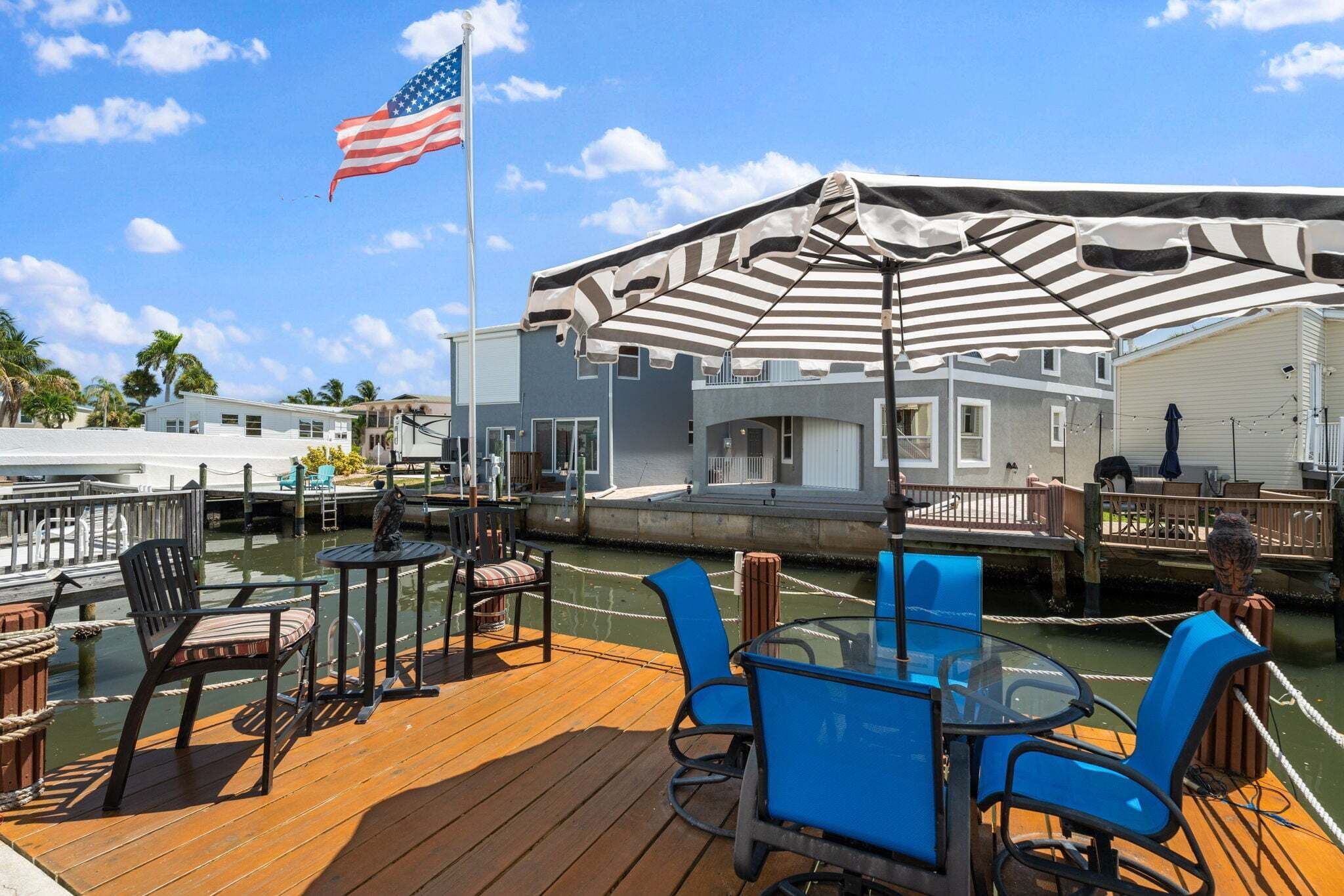 A deck with outdoor seating, a flag, and a building with a striped awning.