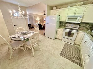 Eine moderne Küche mit weißen Schränken, einem Kühlschrank, einem Backofen und einer Mikrowelle. Ein Esstisch mit Stühlen und eine Chandelier sind ebenfalls vorhanden.