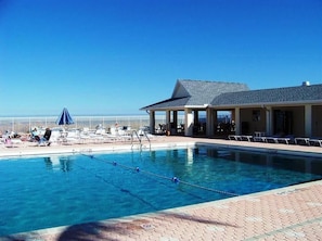 Ein Schwimmbecken mit Liegestühlen und Sonnenschirmen, eine überdachte Sitzgelegenheit und freier Blick auf den Strand.