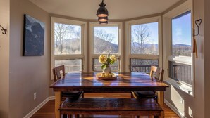A dining area with a wooden table, chairs, a vase with flowers, and a pendant light. - Misty Mountain Hideaway (Blowing Rock)