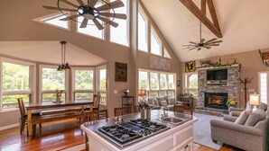 A spacious living area with a fireplace, large windows, and a kitchen island. - Misty Mountain Hideaway (Blowing Rock)