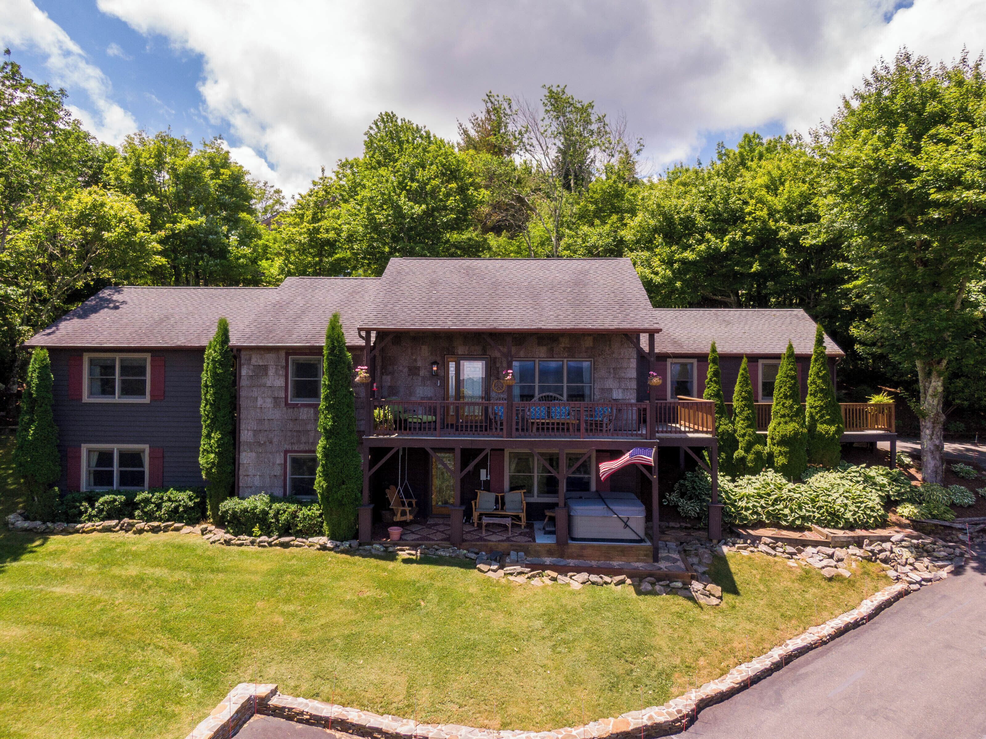 A two-story house with a deck, stone exterior, and a well-maintained lawn.
