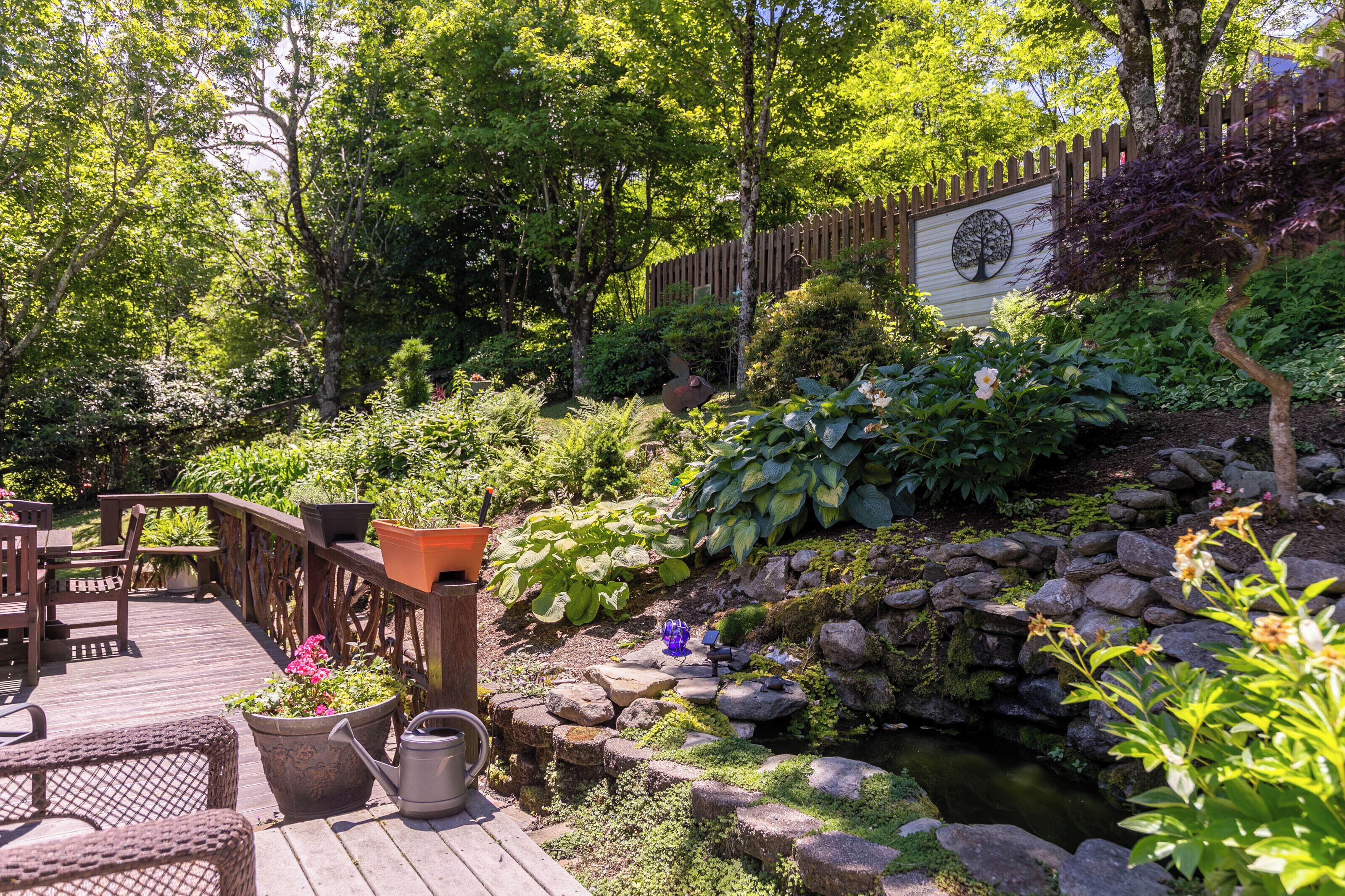 A wooden deck with outdoor furniture, a small garden with a pond, and a wooden fence.