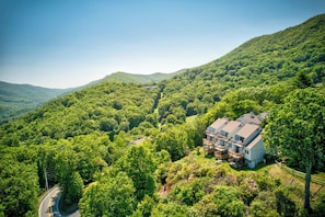 A house surrounded by dense forest, with a road curving through the landscape. - Top Of Seven 2BR - Amazing Grandfather Mtn Views From This Updated Condo (Banner Elk)