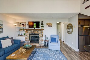 A living room with a stone fireplace, a blue sofa, a coffee table, and a blue armchair.