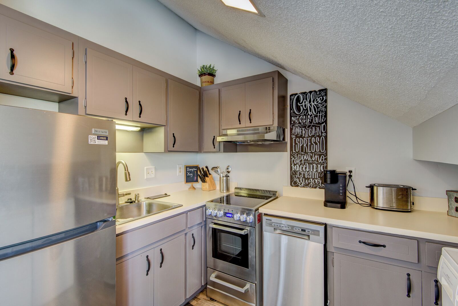 A compact kitchen with stainless steel appliances, a coffee machine, and a chalkboard menu.