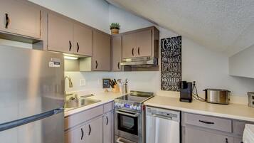 A compact kitchen with stainless steel appliances, a coffee machine, and a chalkboard menu.