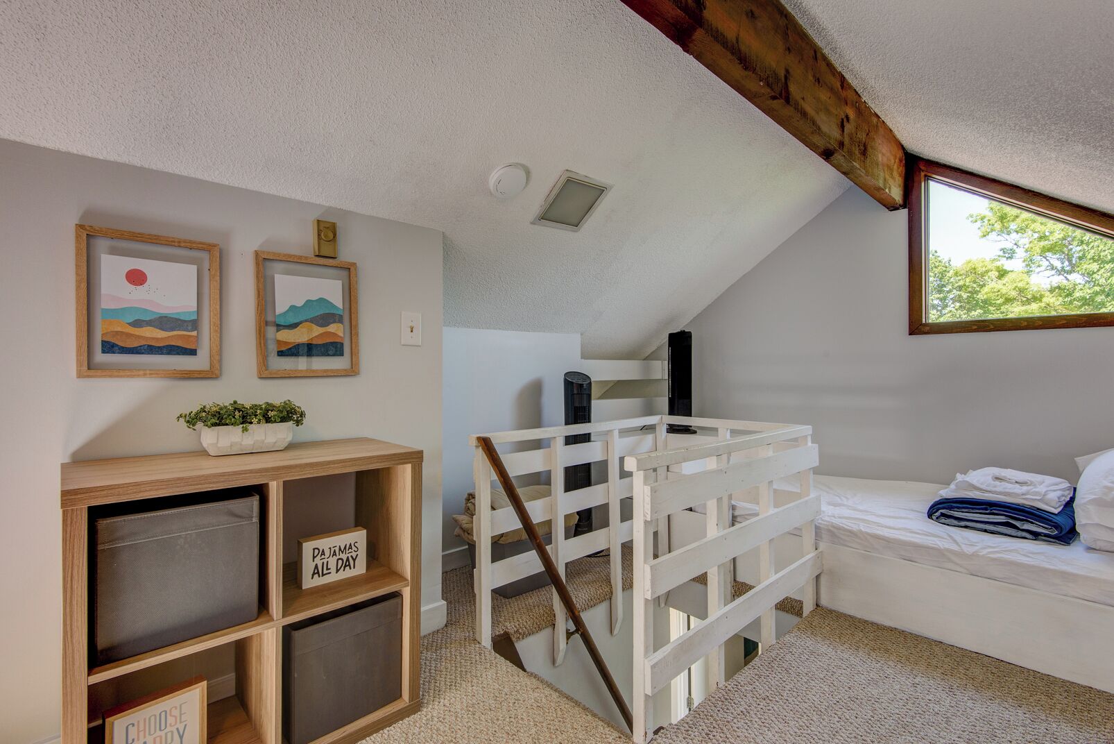 A cozy attic bedroom with a sloped ceiling, a white bed, a wooden shelf with a sign, and two framed pictures on the wall.