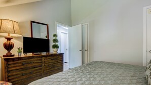 Een slaapkamer met een bed, een dressoir, een televisie en een spiegel.