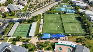 An aerial view of a residential area with a tennis court, a pool, and surrounding houses. - Beachbound 2BR Apt 1282 (Jensen Beach)