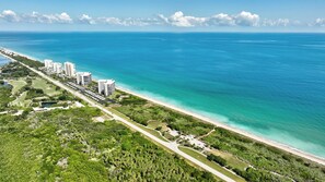 An aerial view of a coastal area with high-rise buildings, a beach, and a golf course. - Beachbound 2BR Apt 1282 (Jensen Beach)