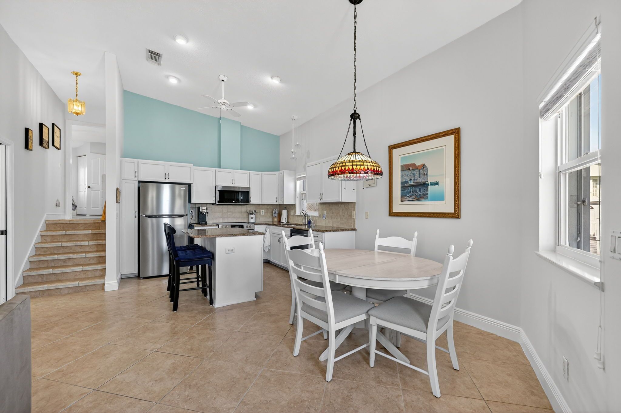 A modern kitchen with white cabinets, a stainless steel refrigerator, and a dining area with a round table and white chairs.