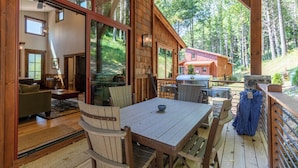 Una baita di legno con zona pranzo, cucina con griglia e ampia finestra vista foresta.
