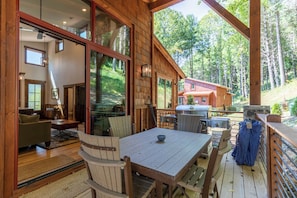 A wooden cabin with a dining area, large windows, and a deck overlooking a forest. - Apres Chalet at Eagles Nest (Banner Elk)
