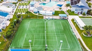 An aerial view of a residential area with a tennis court, swimming pool, and adjacent houses. - Isle Always Luv View 2BR 1277 (Jensen Beach)