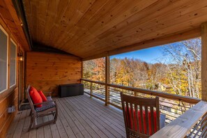 Eine Holzterrasse mit Geländer, eine Bank mit roten Kissen und Blick auf Herbstbäume.