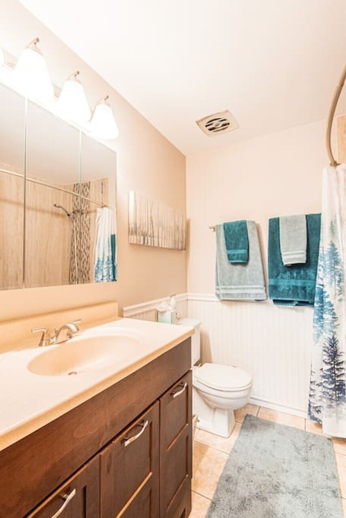 Un baño con tocador de madera, un espejo grande, inodoro y cortina de ducha.