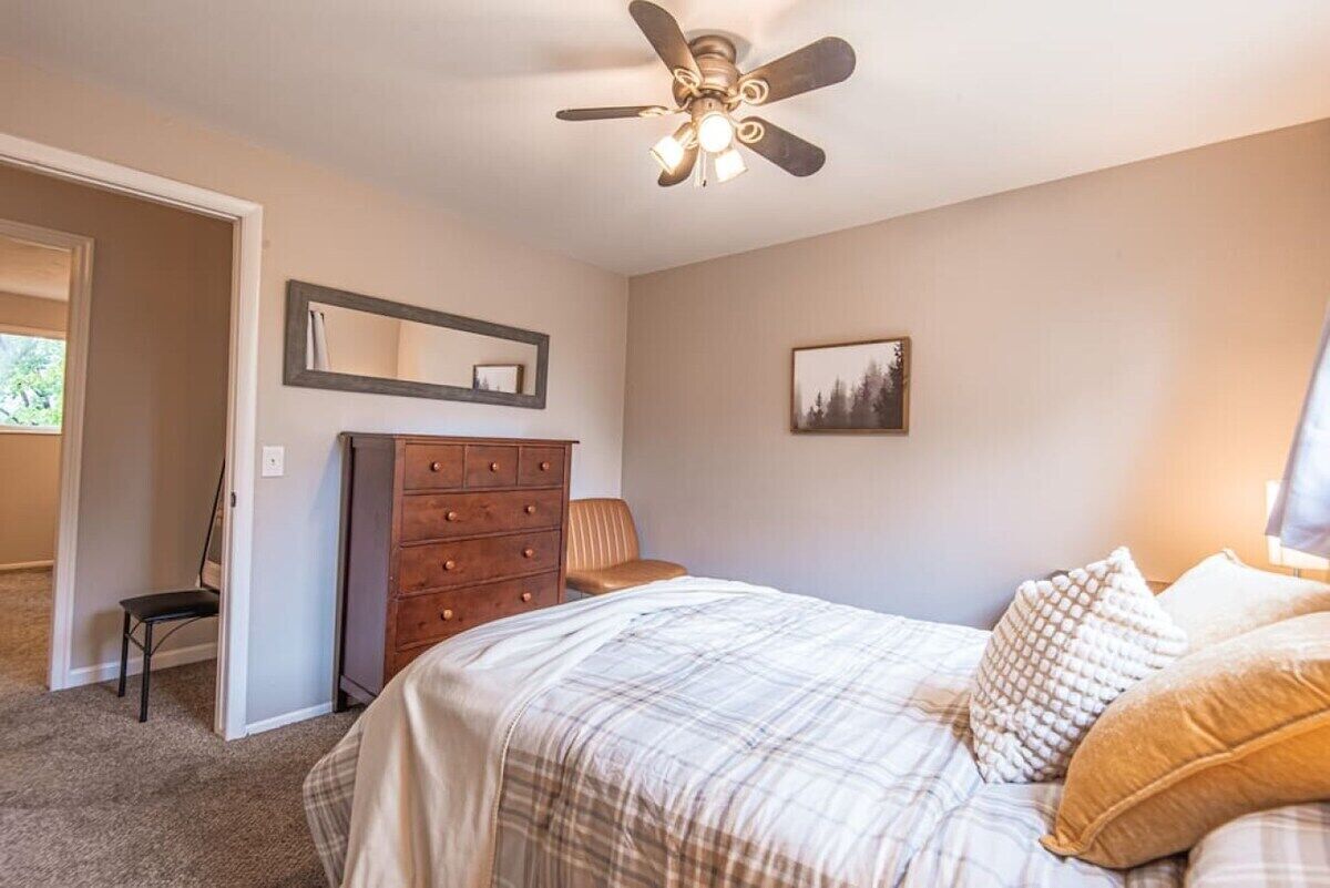 Ein Schlafzimmer mit einem Bett, einem Schminktisch, einem Sessel, einem Deckenventilator und einem gerahmten Bild an der Wand.