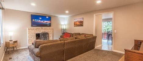 A living room with a fireplace, a large sectional sofa, a flat-screen TV, and a dining area.