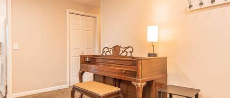 Um quarto com um piano de madeira, um banco, uma mesinha e uma estante fixada na parede com prendedores.
