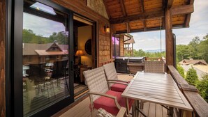 Um deck de madeira com mobiliário externo, uma porta de vidro que dá para um pátio e vista para a paisagem ao redor.