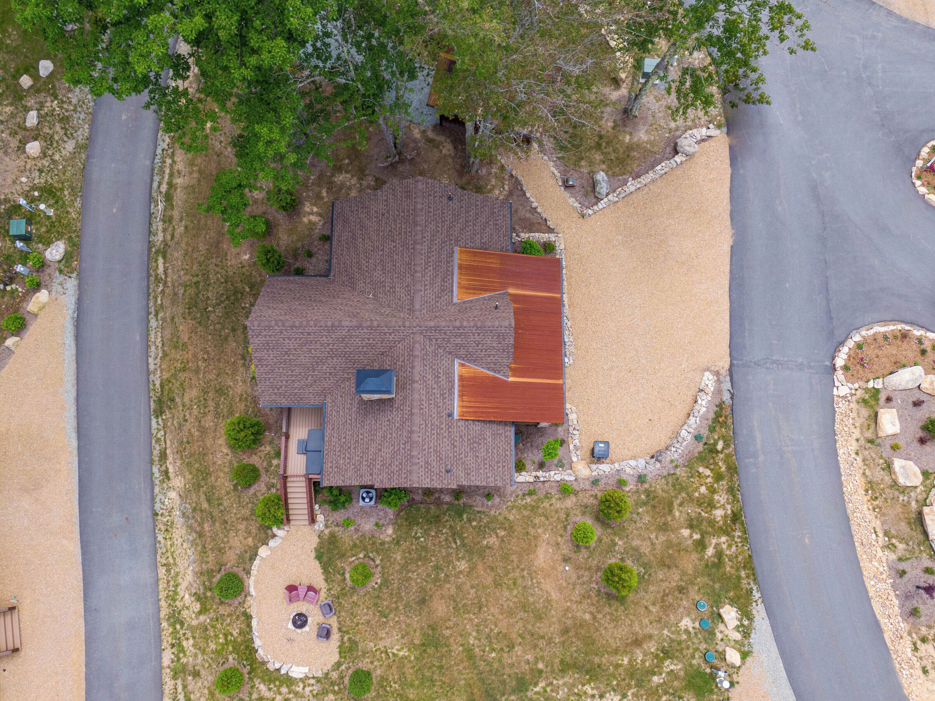 Una vista aerea di una casa con tetto a falde, un portico e un giardino curato con un braciere e un'area salotto.
