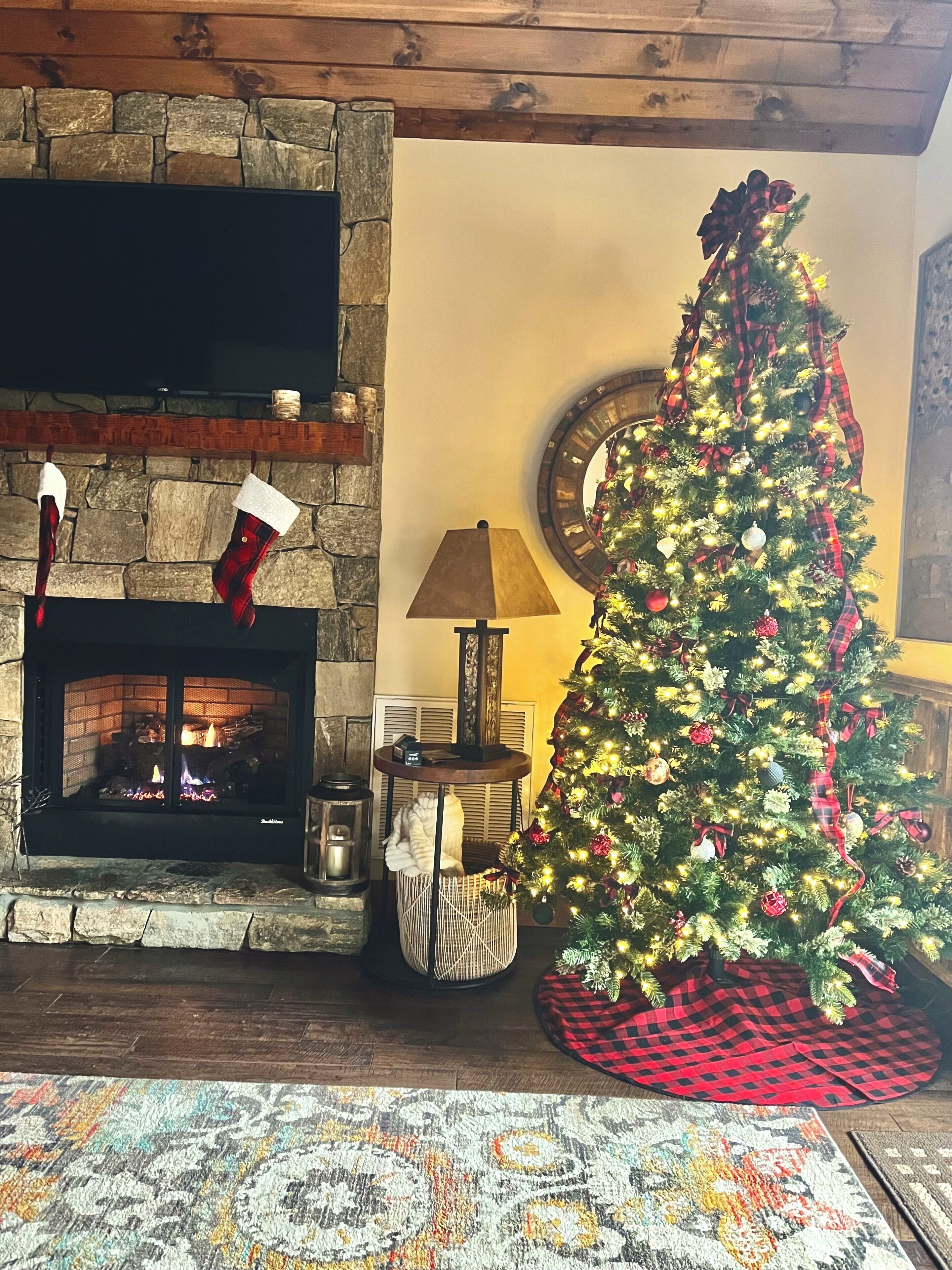 A fireplace with stockings, a Christmas tree, and a lamp.