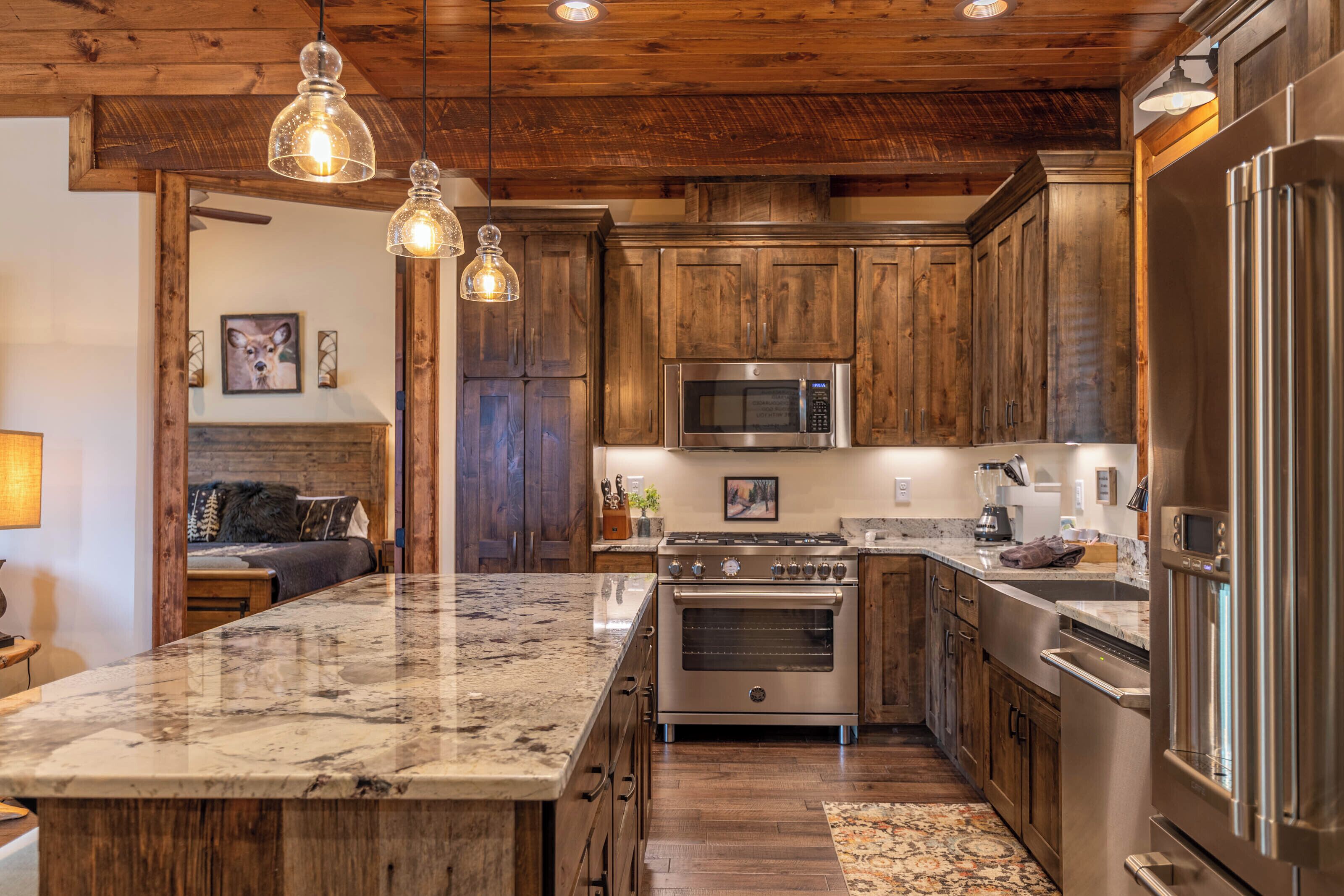 A kitchen with wooden cabinets, stainless steel appliances, a marble countertop, and pendant lighting.