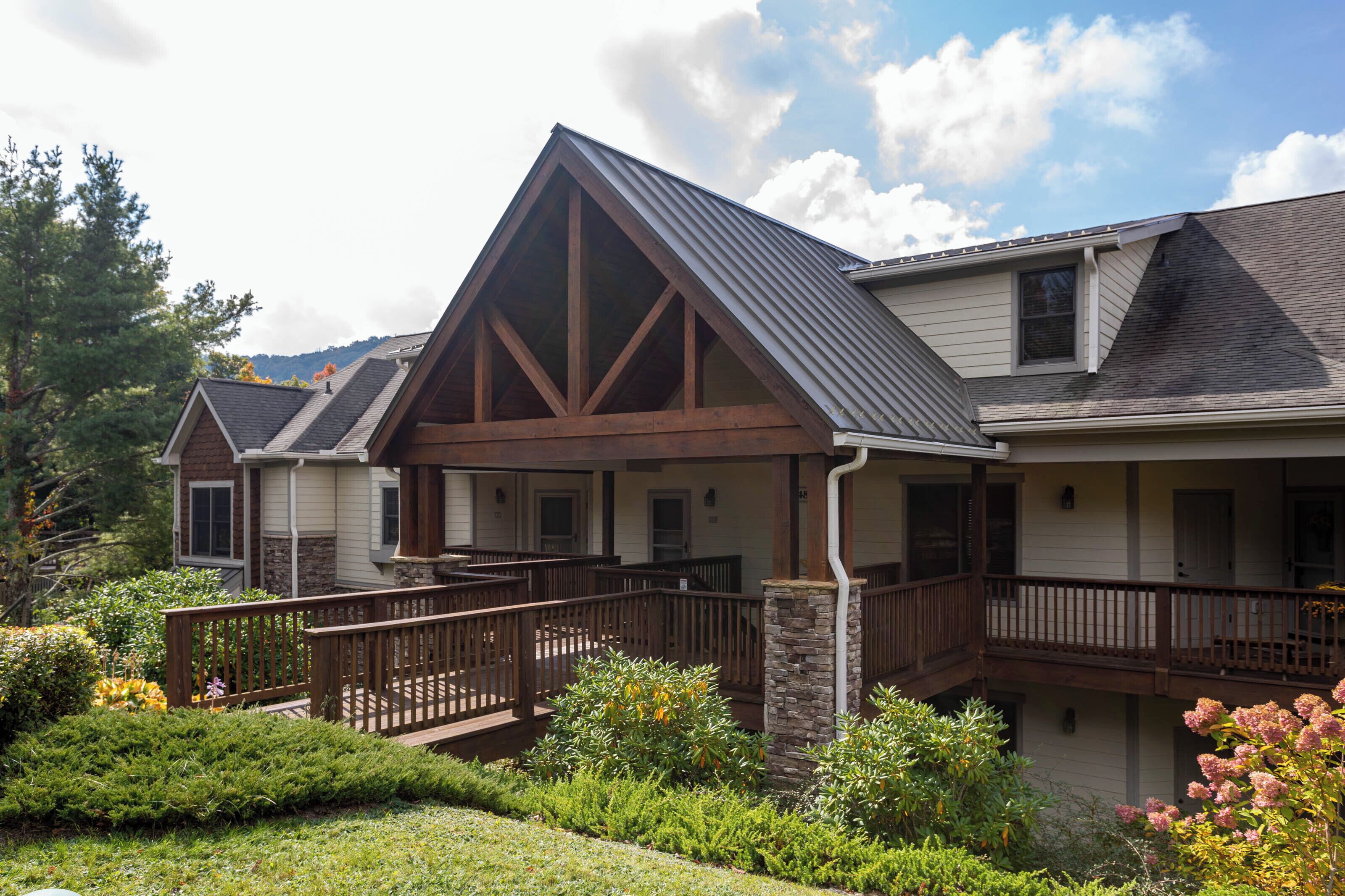 A two-story house with a prominent gable roof, a stone pillar, and a wooden deck.