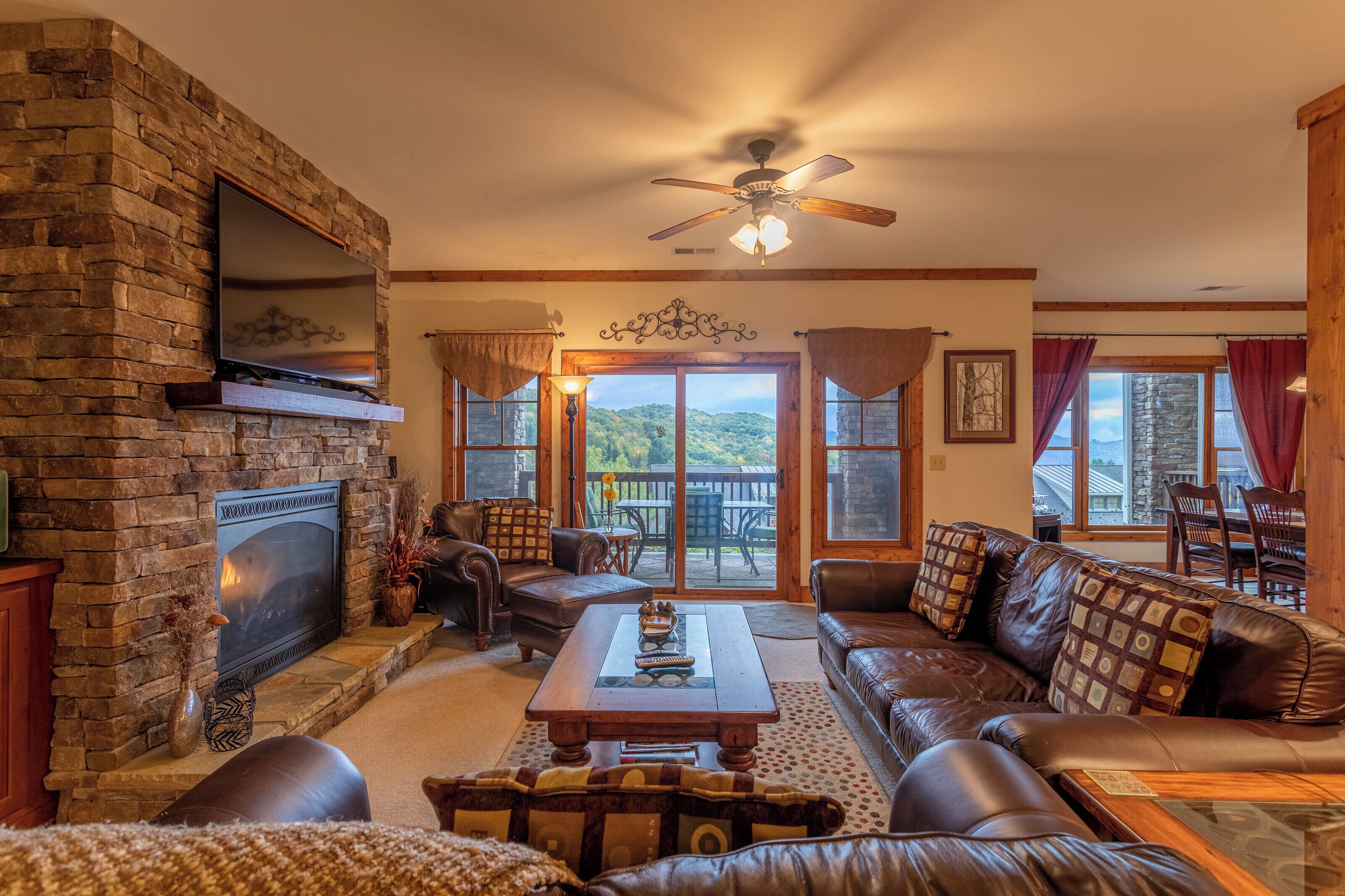 A cozy living room with a stone fireplace, leather furniture, and a view of the outdoors.