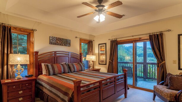 A bedroom with a large bed, two bedside tables, a ceiling fan, and a balcony with a view of trees. - Caribou Crossing at The Lodges at Elkmont (Banner Elk)