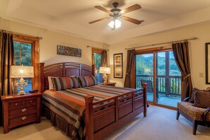 A bedroom with a wooden bed, two bedside tables with lamps, a ceiling fan, and a view of a balcony.