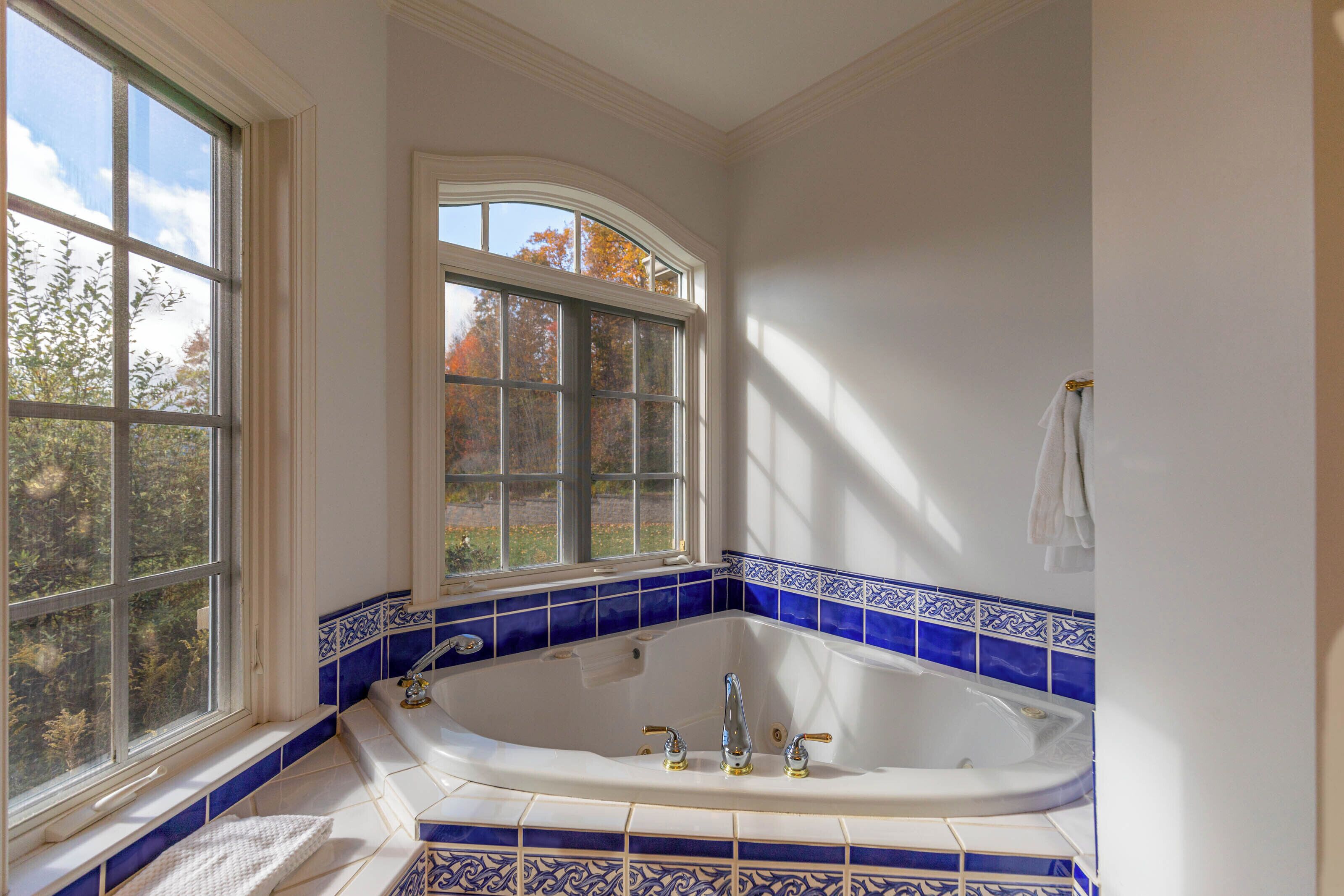 Une salle de bain avec une grande baignoire, une fenêtre et des murs recouverts de carreaux bleus.