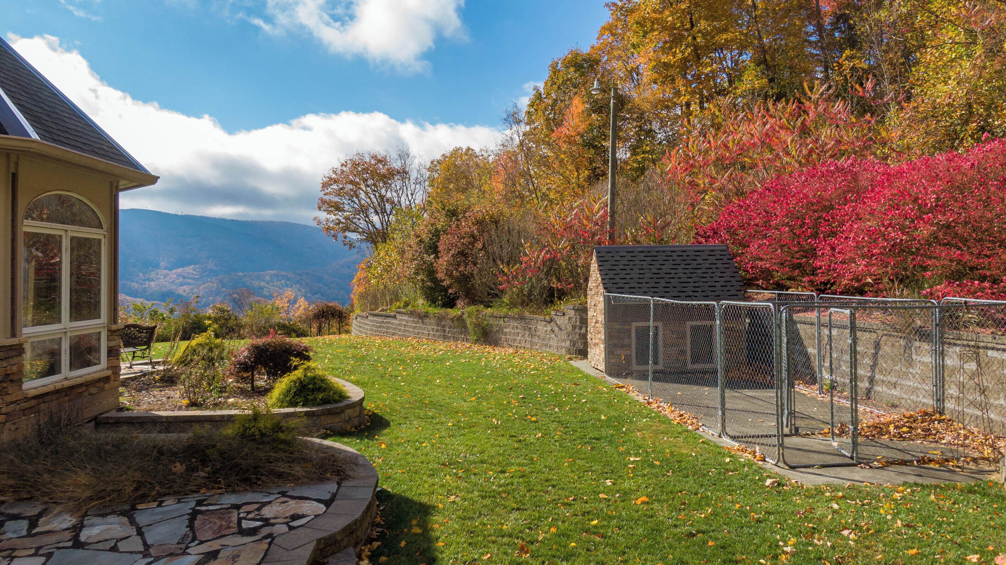 A house with a stone foundation, a stone pathway, a fenced garden, and a view of a mountain range.