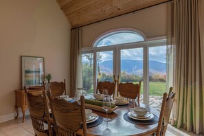 Ein Essbereich mit einem Tisch für vier Personen, Holzsesseln und Blick auf Berge durch große Fenster.