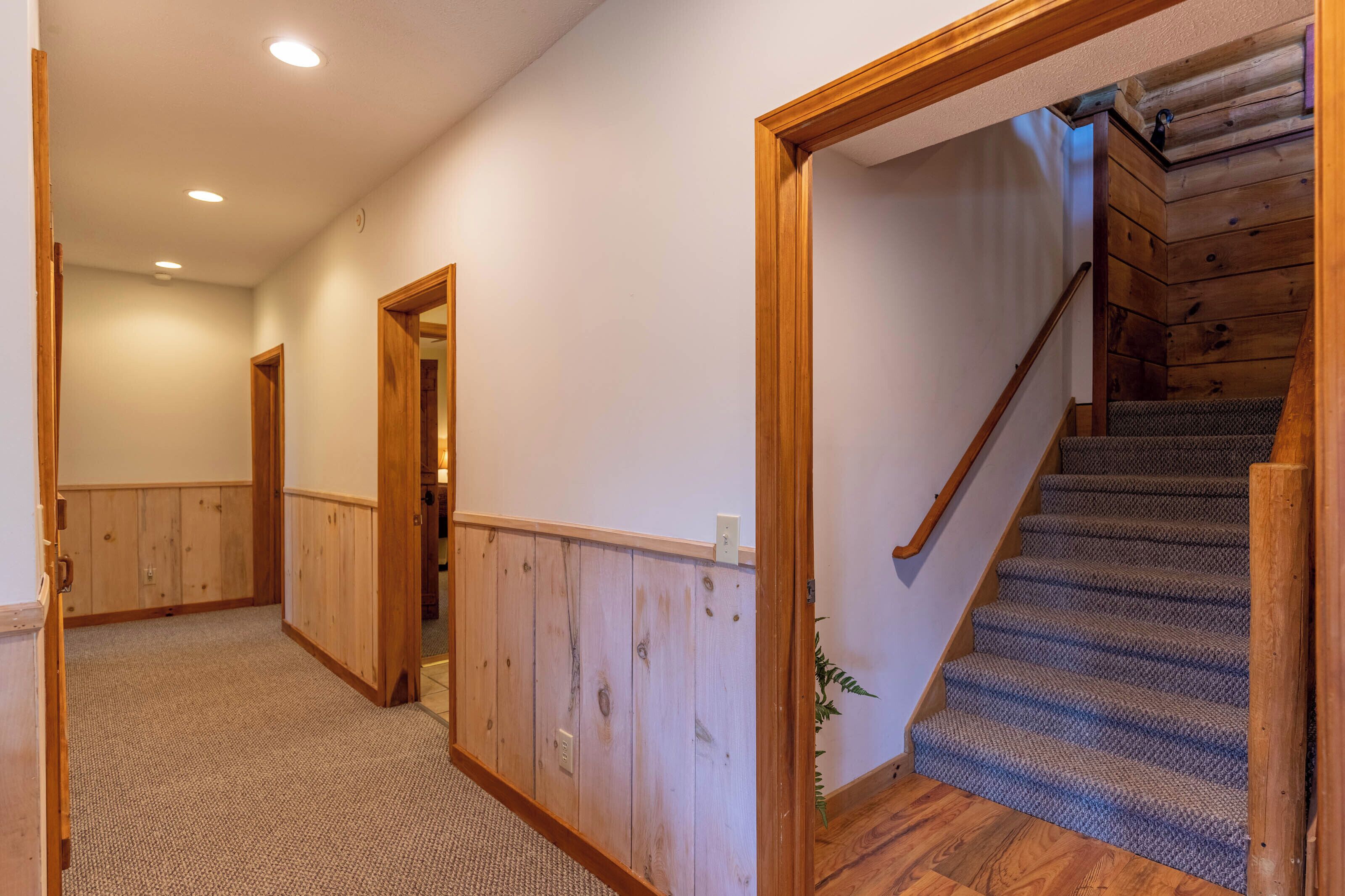 A hallway with wooden paneling, a carpeted floor, and a staircase with a wooden handrail.