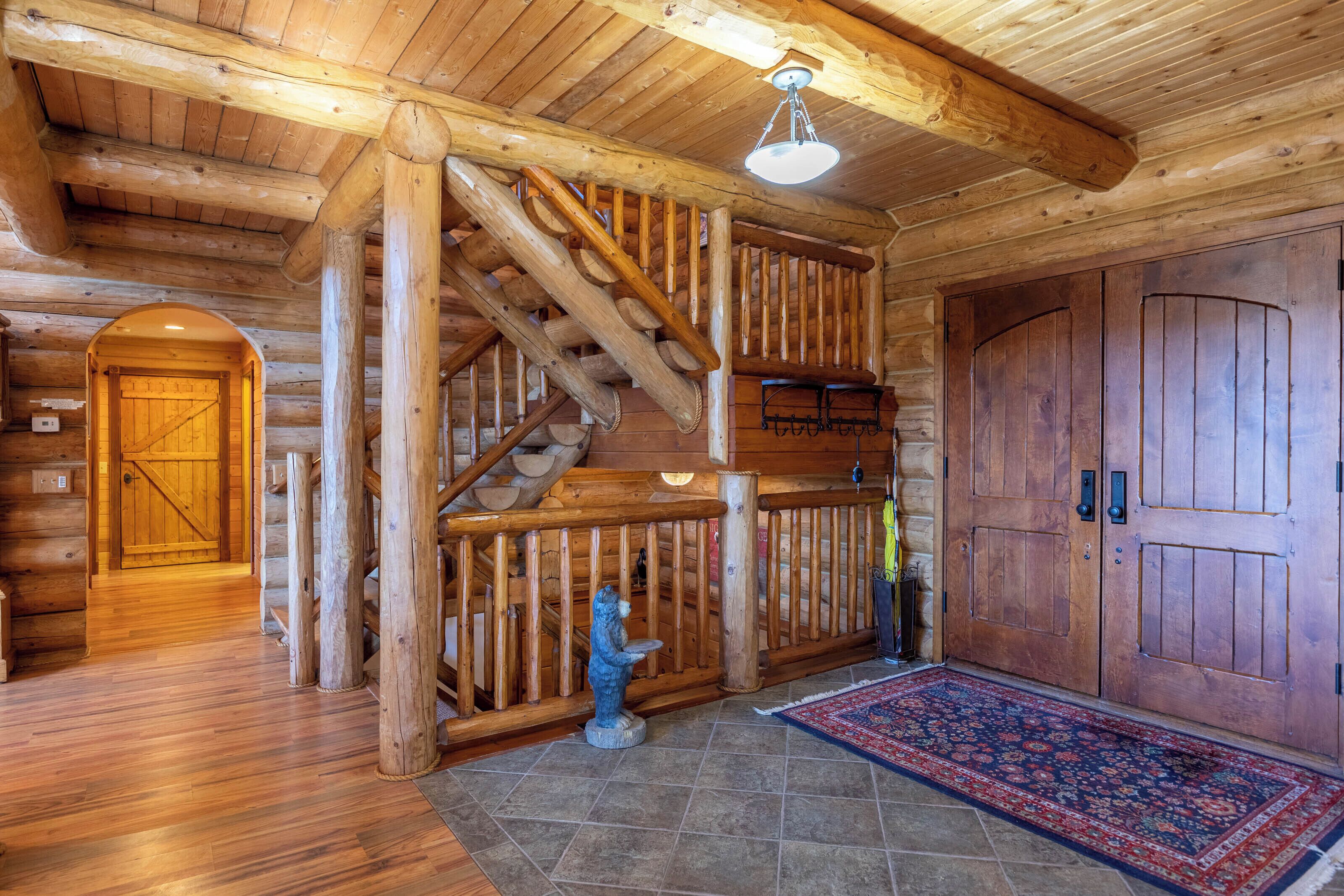 A wooden interior with a staircase, a bear statue, and a large wooden door.
