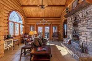 A log cabin interior with a fireplace, wooden furniture, and large windows. - Bear Lodge at Misty Mountain Pet Friendly Luxury Log Cabin With Grandfather Views! (Blowing Rock)