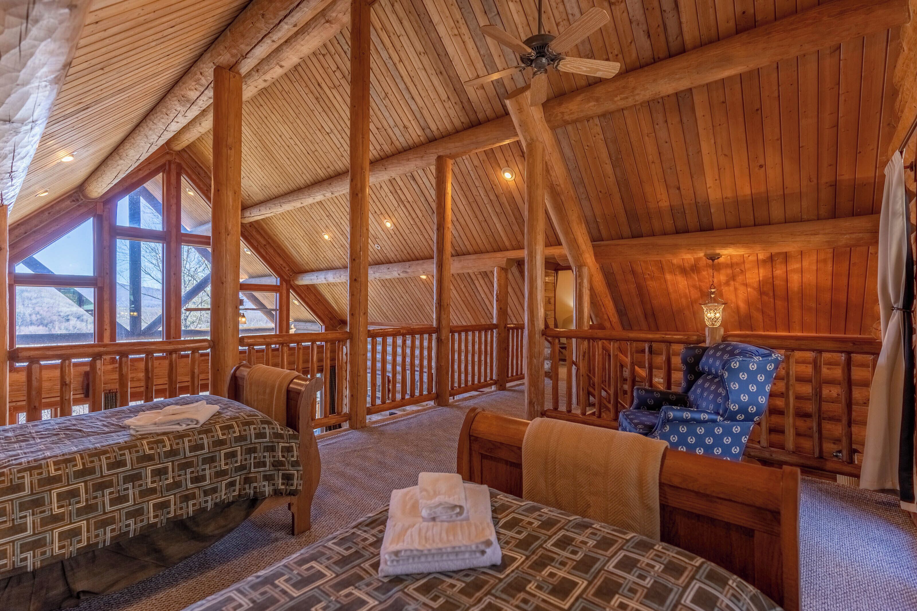 Interior acogedor de una cabaña de troncos con techo alto, vigas de madera, una cama, una mesa con un control remoto y una silla.