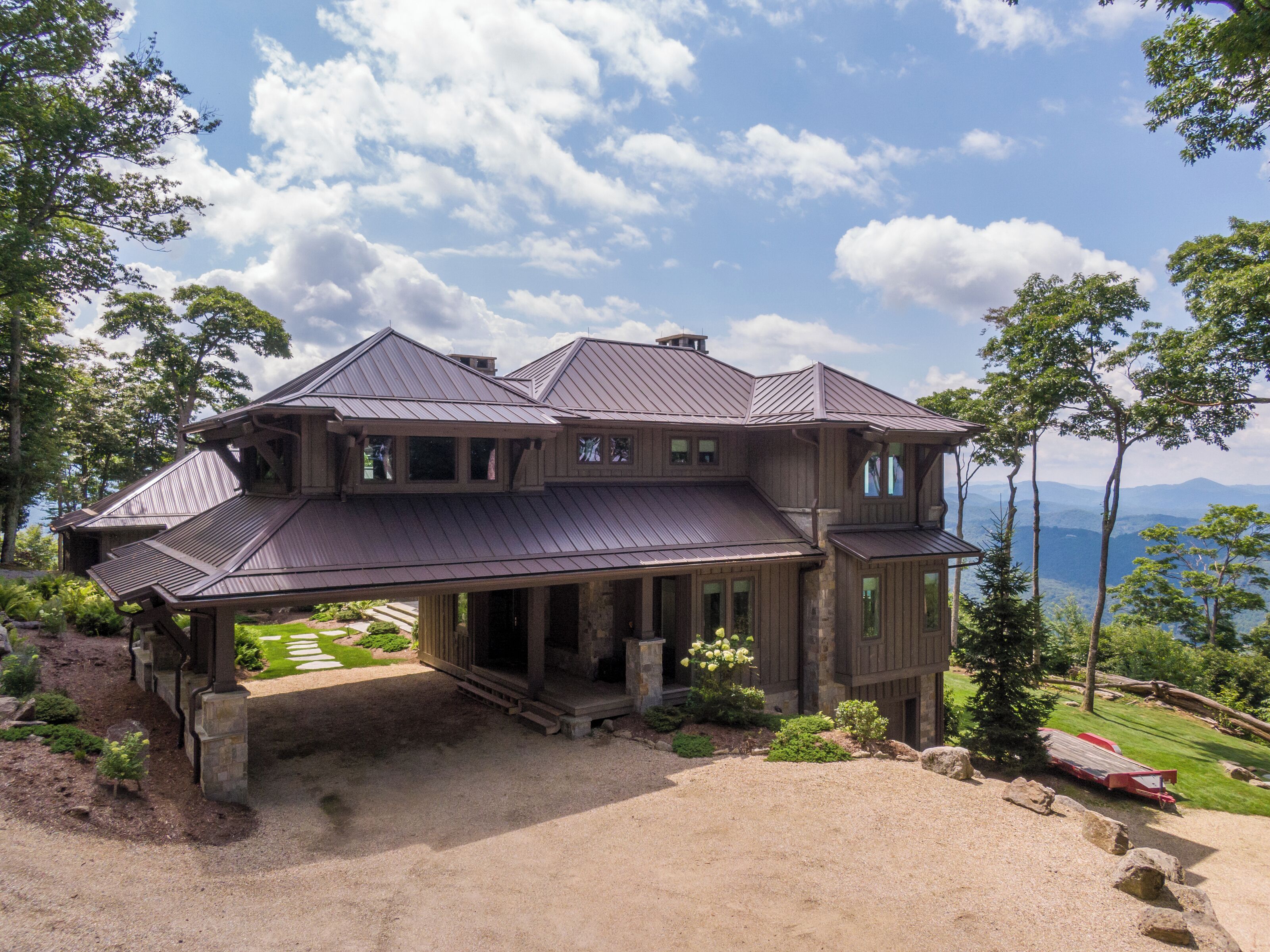 Uma casa grande, de vários andares, com varanda frontal imponente, alicerce de pedra e vista panorâmica da paisagem ao redor.