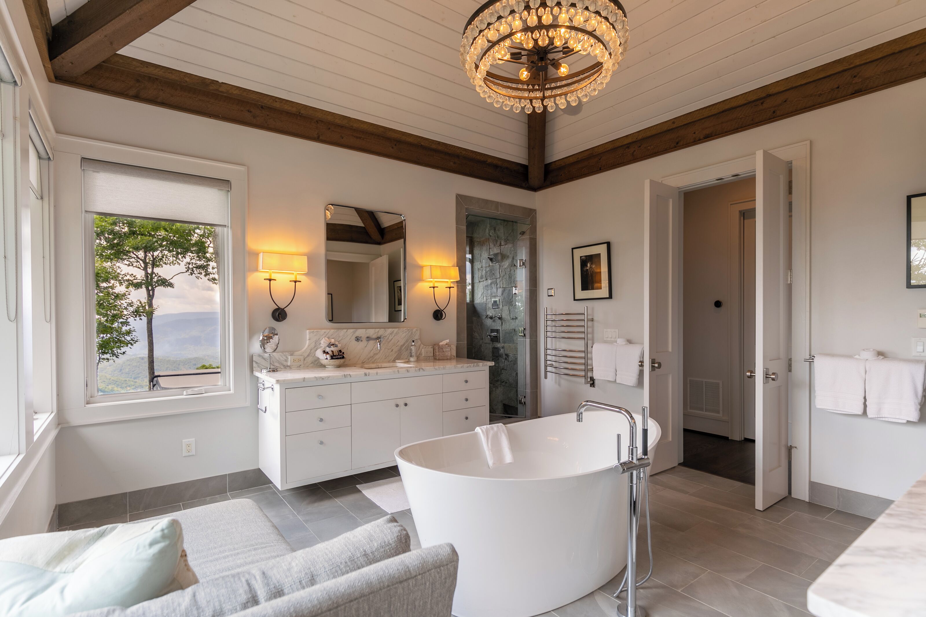 Une salle de bain moderne avec une baignoire sur pieds, un grand miroir et un lustre.