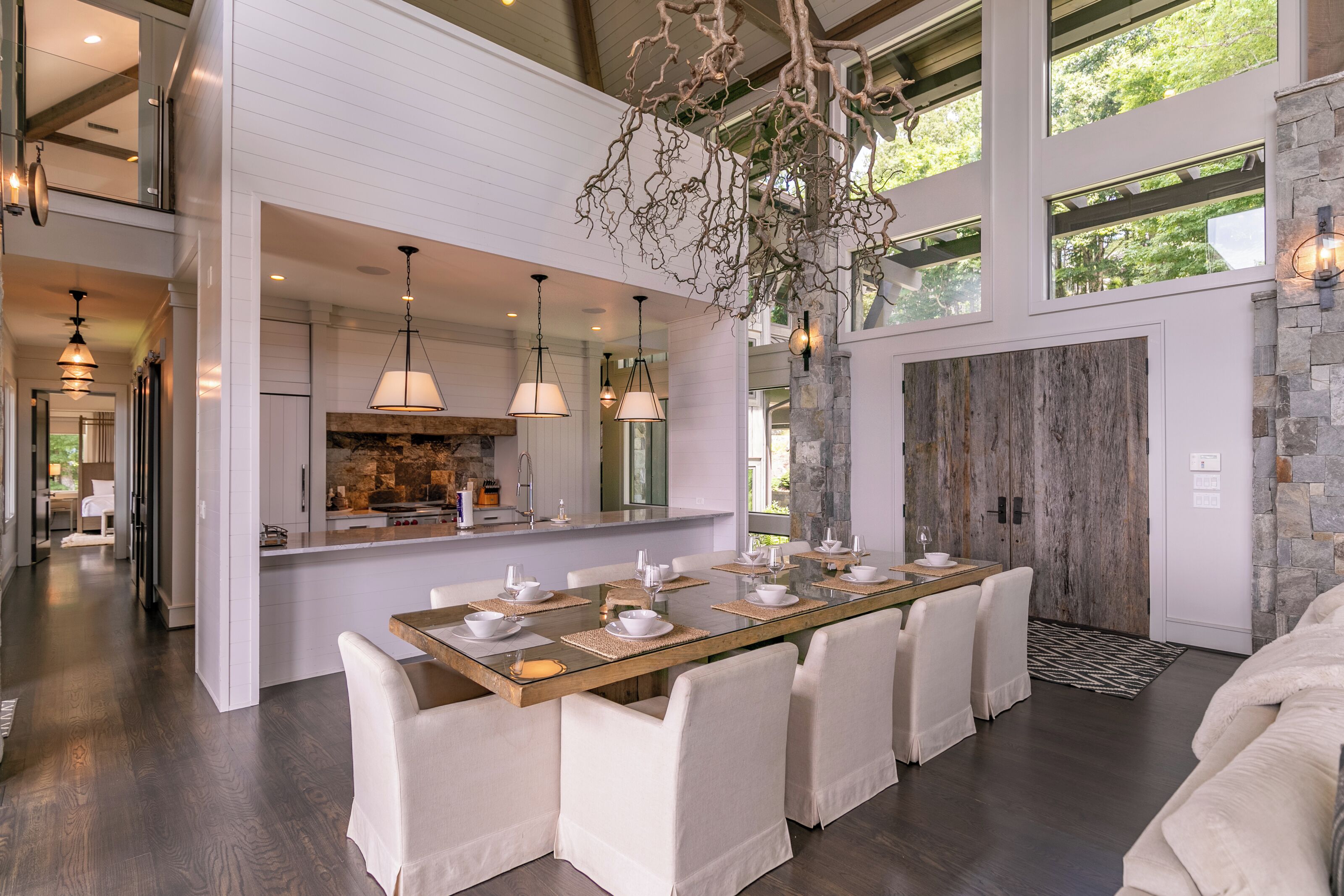 A spacious dining area with a long table, white chairs, and pendant lighting.