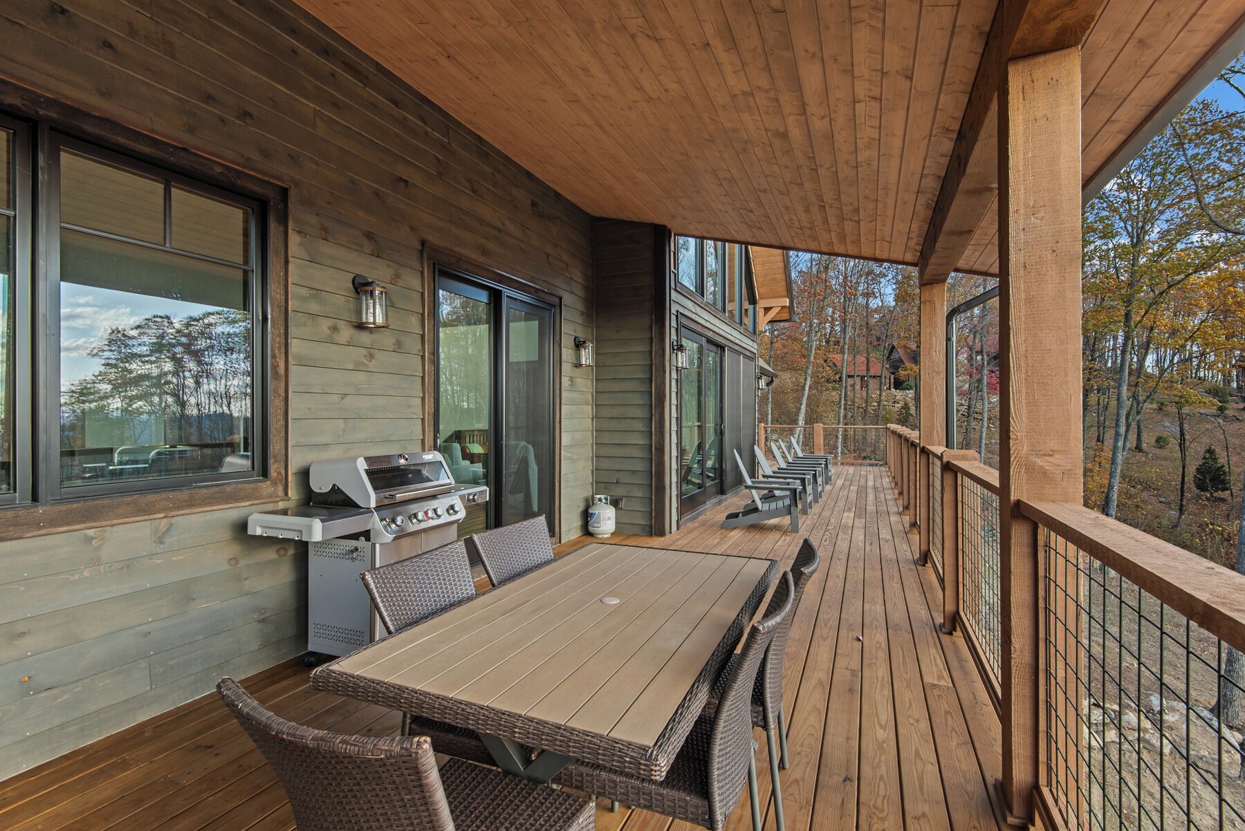 Eine Holzterrasse mit Grill, Esstisch und Stühlen.