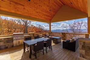An outdoor deck with a grill, seating, and a view of autumn trees and mountains.